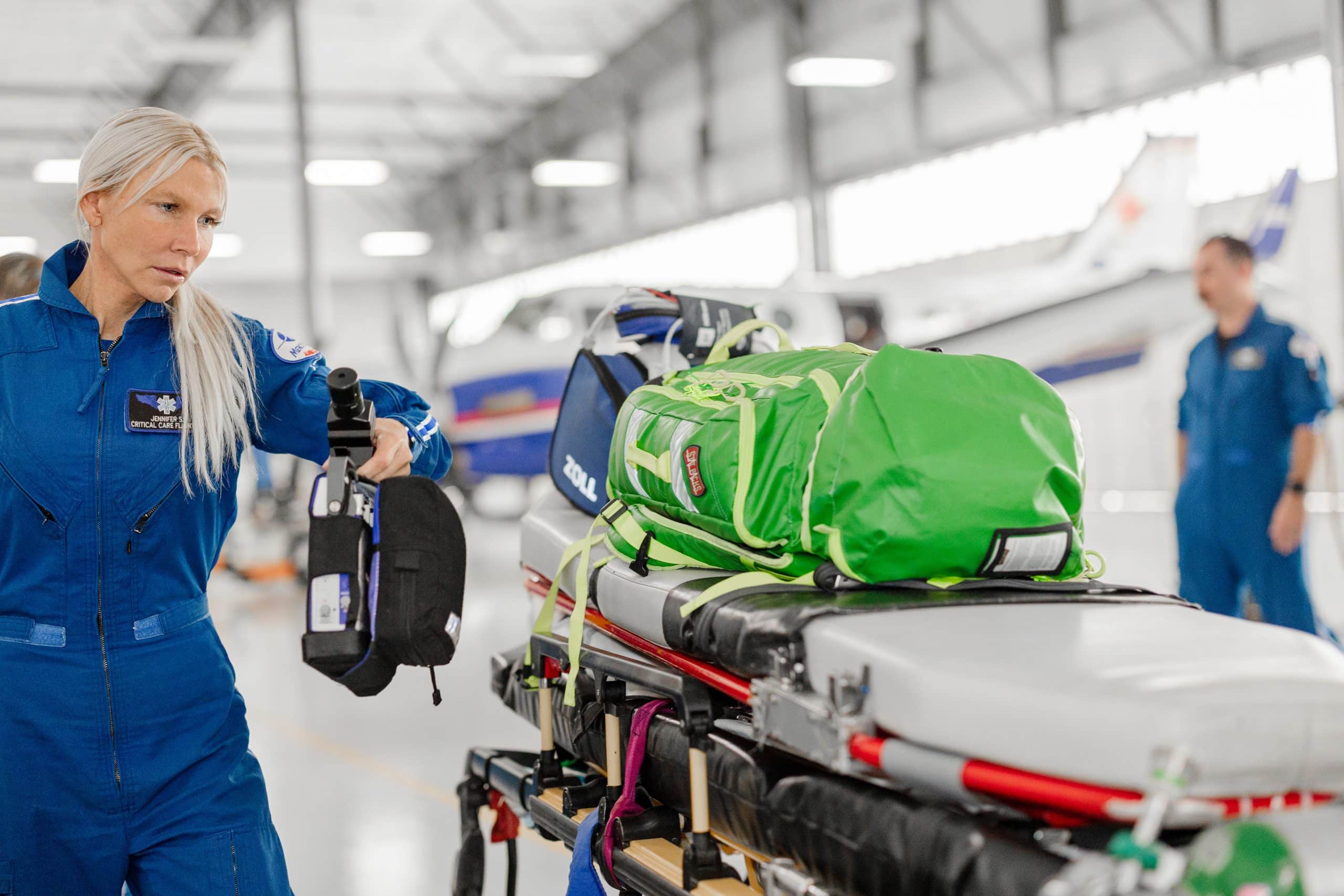 An airline crew member prepares the Searle Starter for aircraft engine start, with a spacious hangar and other crew members in the background, emphasizing aviation maintenance and safety.