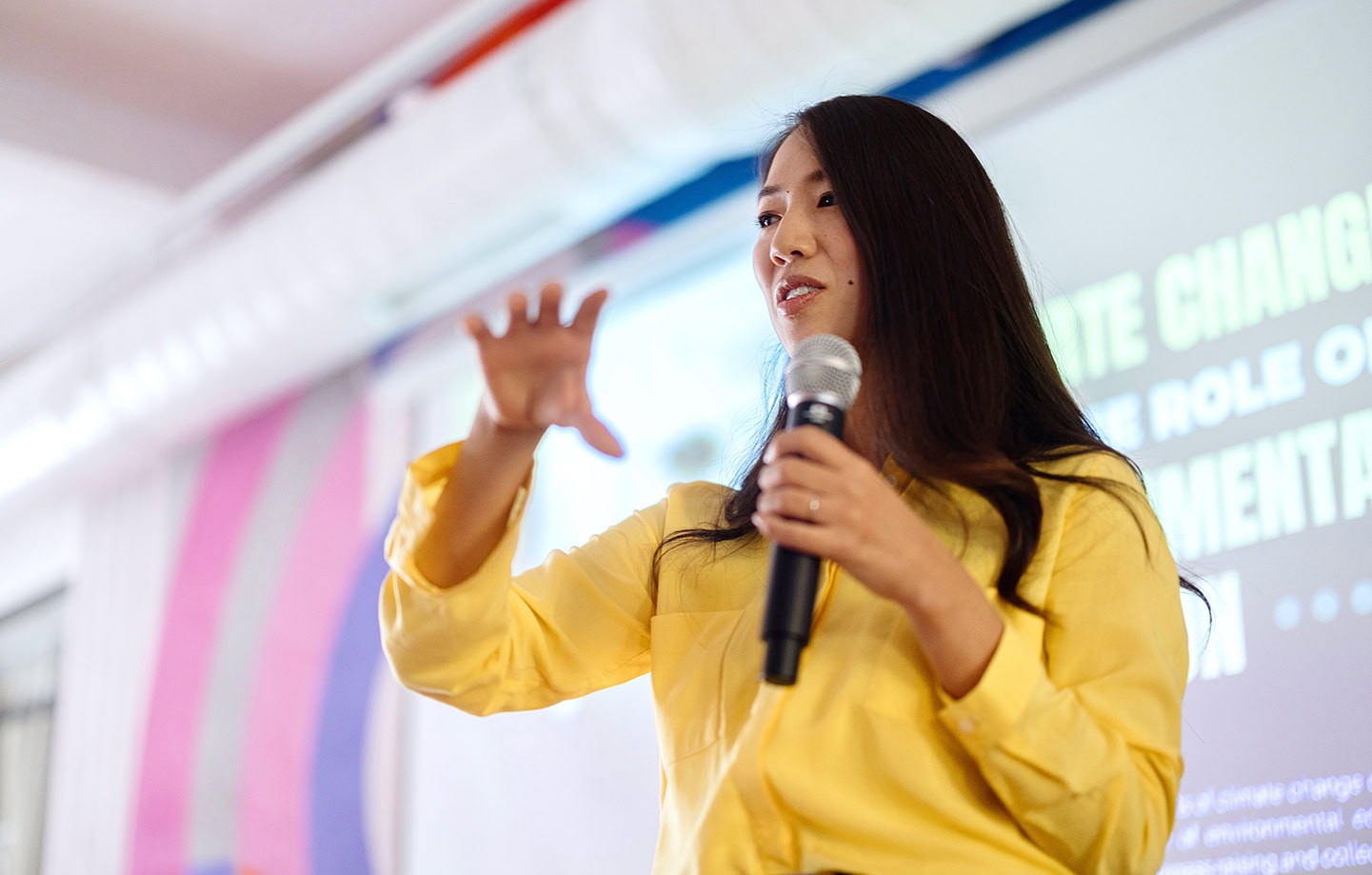 Woman in yellow shirt giving a presentation with a microphone at Searle Starter event, engaging audience on home improvement and community development topics.