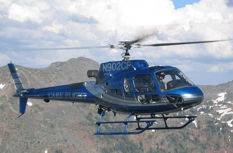 A blue CareFlight Searle Starter helicopter flying over mountainous terrain, showcasing emergency medical transport capabilities for the CareFlight service.