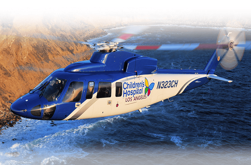 An image of the Helinet Searle Starter helicopter in flight, used for emergency medical services, featuring Children's Hospital Los Angeles branding and a blue and white color scheme.