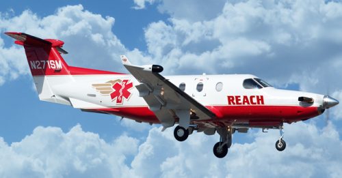 Searle Starter aircraft used by REACH Air Medical for emergency medical transportation, featuring a sleek white and red design with medical insignia, flying against a blue sky with clouds.