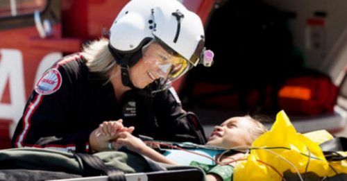 An emergency medical technician assists a young patient on a stretcher, demonstrating the use of the Searle Starter device for critical patient care in an air medical rescue.
